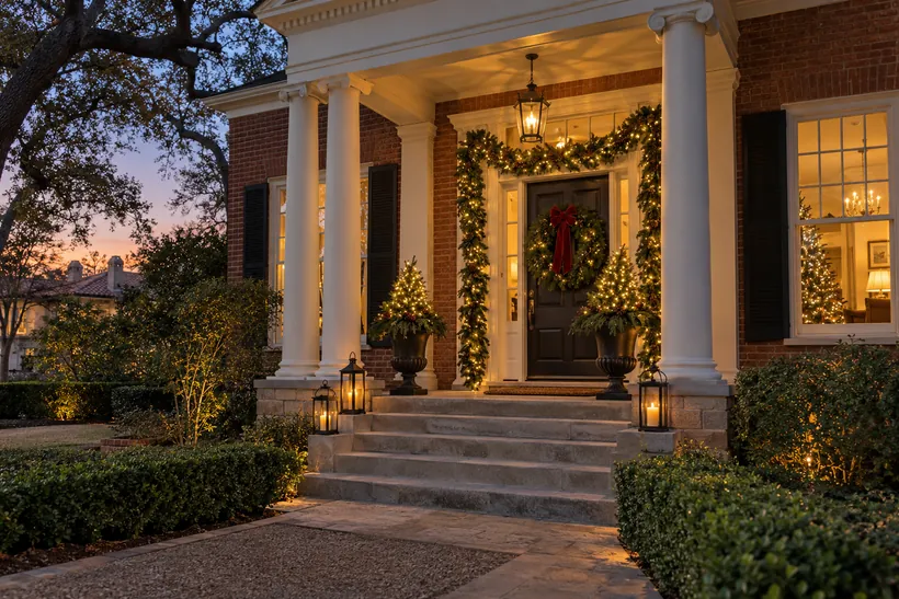 A brick colonial porch with lit garland and a wreath